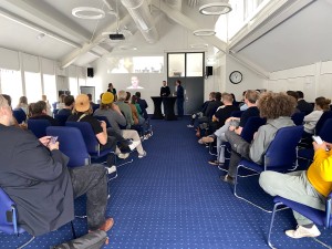 Im Zuge der Veranstaltung „Flensburg digitalisiert“ 2022 sitzen Besuchende in einem bestuhlten Raum und schauen nach vorn zu den Speaker:innen.